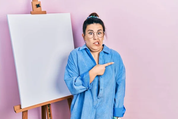 画家のイーゼルのそばに立つ若いヒスパニック系の女性は 前指で心配し 緊張を指摘し 心配し 驚きの表情 — ストック写真
