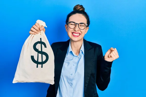 Young Hispanic Girl Wearing Business Clothes Holding Dollars Bag Screaming — 스톡 사진