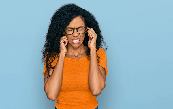 中年非洲裔美国女人穿着休闲装 戴着眼镜 用手指捂住耳朵 对嘈杂的音乐感到恼怒 聋人概念 — 图库照片