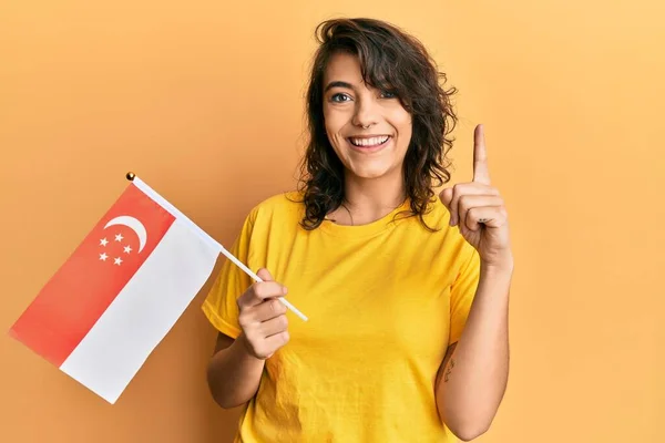 Молода Іспаномовна Жінка Тримає Сінгапурський Прапор Посміхаючись Ідеєю Або Питанням — стокове фото