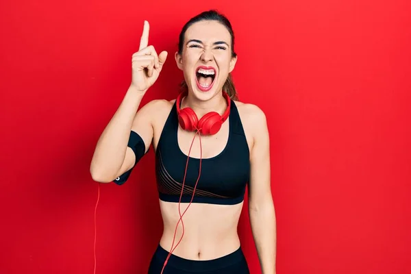 Young Hispanic Girl Wearing Gym Clothes Using Headphones Pointing Finger — ストック写真