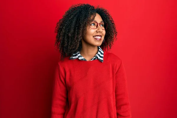 Beautiful african american woman with afro hair wearing sweater and glasses looking away to side with smile on face, natural expression. laughing confident.