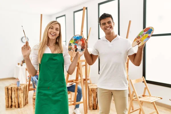 Group of people drawing at art studio. Man and woman smiling happy holding paintbrush and palette.