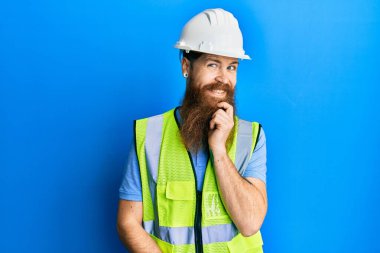 Uzun sakallı, güvenlik kaskı takan ve yansıtıcı ceketli kızıl saçlı adam kameraya gülümseyen kolları çapraz ve çenesi havada bakıyor. Olumlu düşünmek. 