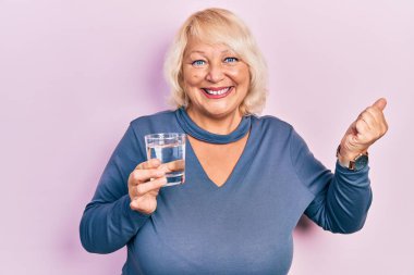 Orta yaşlı sarışın kadın bir bardak su içiyor gururla bağırıyor, zaferi kutluyor ve başarıyı kollarını kaldırarak kutluyor. 