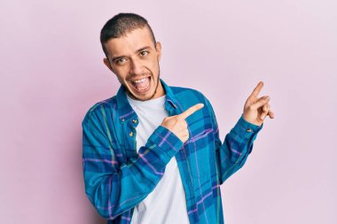 Latin asıllı, sıradan kıyafetler giyen, gülümseyen ve kameraya bakan genç bir adam. İki eliyle ve parmaklarıyla kenarı işaret ediyor.. 