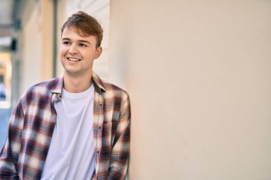 Genç beyaz adam gülümseyerek şehirde mutlu mesut duruyor..