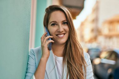 Genç sarışın iş kadını gülümsüyor. Şehirdeki akıllı telefondan konuşuyor..