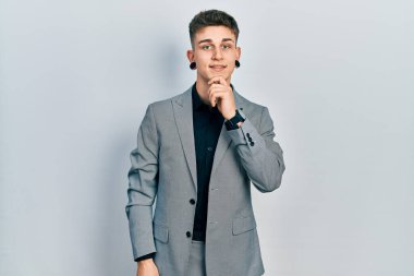 Kulakları genişlemiş, iş ceketi giymiş kolları çapraz ve elleri çenesinde kameraya gülümseyen beyaz bir genç. Olumlu düşünmek. 