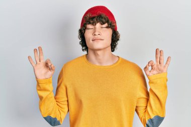 Yün şapkalı yakışıklı genç adam rahatla ve gözleri kapalı gülümse parmaklarıyla meditasyon hareketi yapıyor. yoga konsepti. 