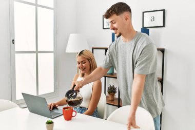 Kadın evde dizüstü bilgisayar kullanıyor ve erkek arkadaşı kahve dolduruyor..