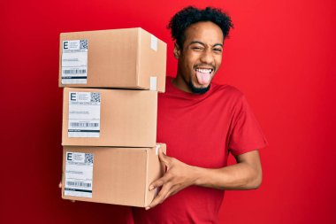 Sakallı, teslimat paketleri taşıyan, dilini mutlu bir ifadeyle dışarı çıkaran genç Afrikalı Amerikalı adam.. 