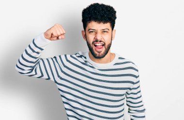 Sakallı, normal çizgili süveter giyen genç bir Arap kızgın ve kızgın bir şekilde yumruğunu kaldırıyor ve öfkeyle bağırıyor. öfke ve agresif konsept. 