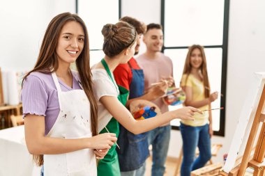 Bir grup insan resim stüdyosunda tuvale resim çizerken mutlu bir şekilde gülümsüyor..