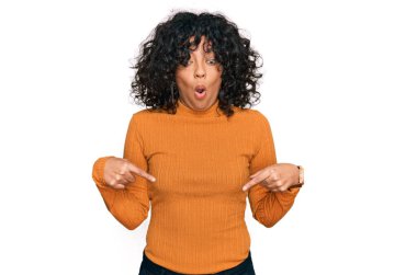 Latin asıllı genç bir kadın, günlük kıyafetler giyip parmaklarını göstererek reklamını yapıyor, şaşırmış yüzünü ve ağzını açıyor. 