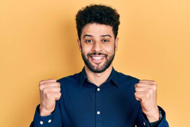 Sakallı, sıradan gömlekli genç bir Arap, kolları açık ve gözleri açık bir şekilde başarıyı kutluyor. Kazanan konsept. 