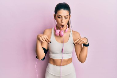 Spor kıyafetleri giyen, kulaklık takan, reklam veren, şaşırmış yüzlü ve ağzı açık genç bir İspanyol kadın. 