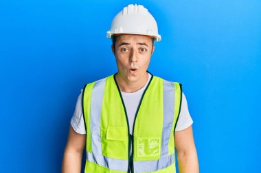 Güvenlik kaskı ve yansıtıcı ceket giyen yakışıklı genç bir adam. Şaşırtmak için ağzı açık kalmış, korkmuş ve hayrete düşmüş. İnanmayan yüz. 