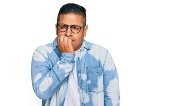 Gündelik kıyafetler ve gözlük takan genç Latin adam gergin ve gergin görünüyor. Ağzı tırnak yiyen eller. anksiyete. 