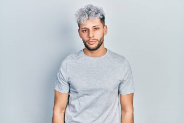 Modern boyalı saçlı, sıradan gri tişörtlü, yüzünde ciddi bir ifadeyle rahatlamış genç bir İspanyol. Basit ve doğal bir şekilde kameraya bakıyorsun.. 