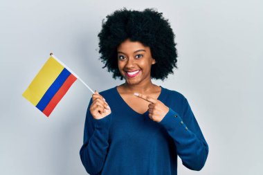 Kolombiya bayrağı tutan genç Afrikalı Amerikalı kadın mutlu bir şekilde el ve parmak işareti yapıyor. 