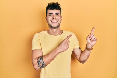 Gündelik tişört giyen genç İspanyol adam gülümseyip kameraya bakıyor ve iki eliyle ve parmaklarıyla kenarı işaret ediyor.. 