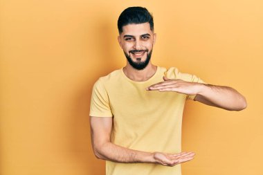 Sakallı, sıradan sarı tişörtlü, elleri büyük ve büyük boy işareti gösteren yakışıklı bir adam. Kameraya bakıp gülümsüyor. ölçüm kavramı. 