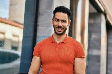 Genç İspanyol adam gülümseyerek şehirde mutlu mesut dikiliyor..