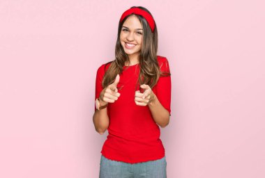 Genç esmer kadın, gündelik giysiler içinde mutlu ve komik yüzüyle kamerayı işaret ediyor. iyi enerji ve titreşimler. 