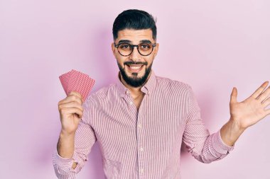 Poker kartları tutan yakışıklı adam başarıyı mutlu bir gülümsemeyle kutluyor ve kazanan el kaldırarak ifade ediyor. 