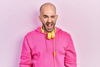 Spor kıyafetleri giyen ve kulaklık takan genç kel bir adam kameraya seksi bir ifadeyle bakıyor, neşeli ve mutlu bir yüzle.. 