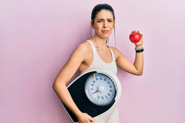 Young Hispanic Woman Wearing Sportswear Holding Weighing Machine Apple Clueless — ストック写真