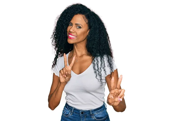 中世のアフリカ系アメリカ人女性は 勝利のサインをする指を示すカメラを見て笑顔カジュアルな白いTシャツを着ていた — ストック写真