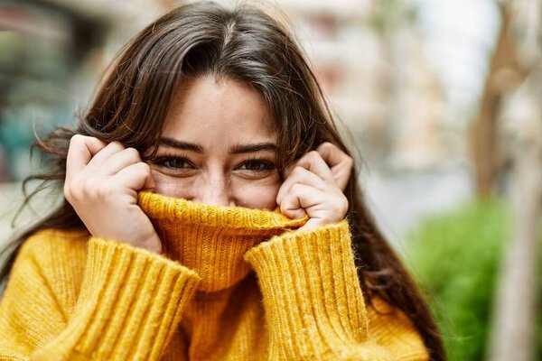 Young beautiful brunette woman wearing turtleneck sweater doing funny gesture covering face with sweater