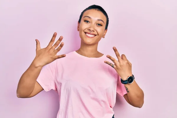 自信と幸せ笑顔ながら カジュアルなピンクのTシャツを着て 指の数8で指摘しながら短い髪を持つ美しいパニック女性 — ストック写真