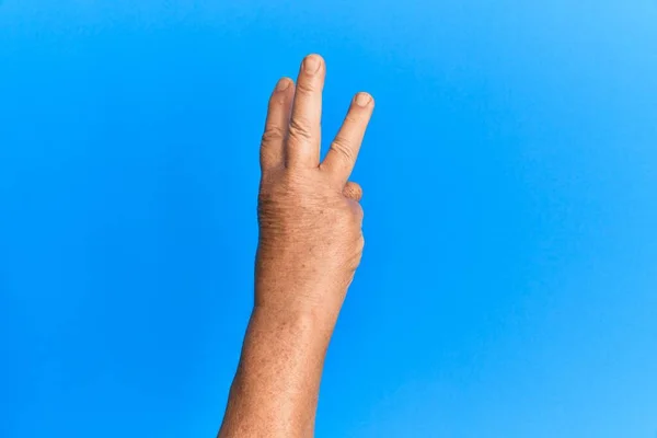 Рука Старшого Іспаномовного Чоловіка Над Синім Ізольованим Тлом Підрахунок Номер — стокове фото