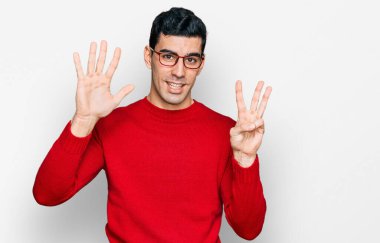 Yakışıklı İspanyol bir adam günlük kıyafetler ve gözlük takıyor. Sekiz numaralı parmaklarıyla gösteriyor ve işaret ediyor. Kendinden emin ve mutlu.. 