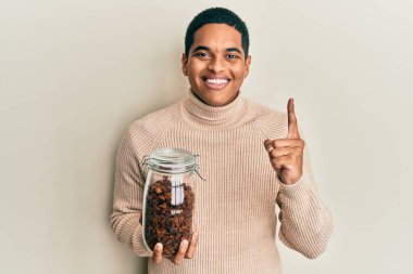 Genç, yakışıklı, elinde kuru üzümlerle dolu bir kavanoz tutan ve gülümseyen bir adam. 