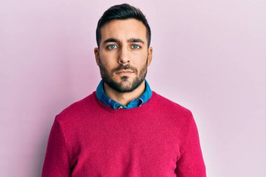 Günlük kıyafetler giyen genç İspanyol adam yüzünde ciddi bir ifadeyle rahatlamış. Basit ve doğal bir şekilde kameraya bakıyorsun.. 