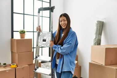 Genç Çinli kız gülümsüyor mutlu bir şekilde yeni evinde merdiven tutuyor.