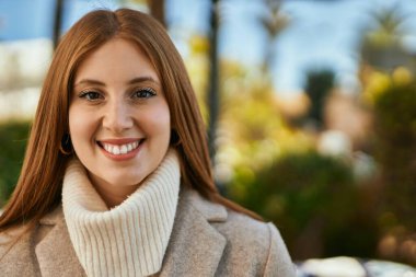 Genç kızıl kız gülümsüyor, mutlu bir şekilde şehirde duruyor..