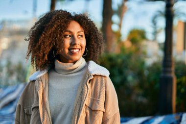 Genç Afrikalı Amerikalı kadın gülümseyerek şehirde mutlu mesut duruyor..