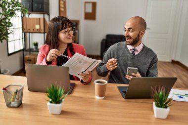 Ofiste bilgisayar ve akıllı telefon kullanarak çalışırken gülümseyen iki İspanyol iş adamı..