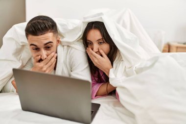 Yatakta dizüstü bilgisayar kullanarak film izleyen genç İspanyol çift..