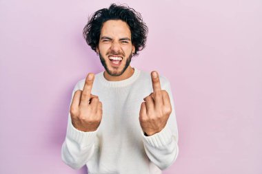 Handsome hispanic man wearing casual white sweater showing middle finger doing fuck you bad expression, provocation and rude attitude. screaming excited 