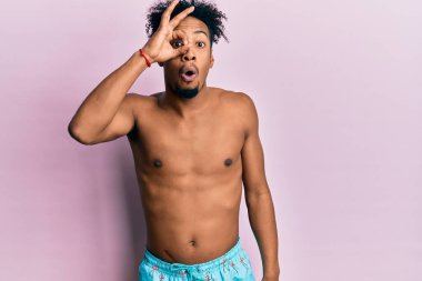 Sakallı, mayo giyen, şaşırmış yüzüyle şaşırmış, parmaklarından bakan Afro-Amerikan bir adam. İnançsız ifade. 