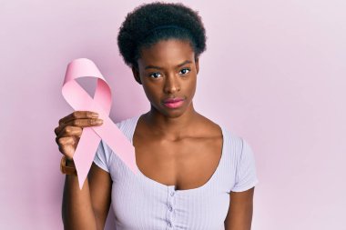 Genç Afrikalı Amerikalı kız pembe kanser kurdelesi takıyor. Düşünme tavrı ve ayık yüz ifadesi. Kendine güveni tam görünüyor. 