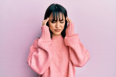 Kâküllü genç esmer kadın stresten dolayı elleri başının üstünde, günlük kışlık süveter giyiyor. migren ağrısı. 