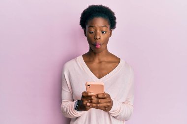 Genç Afrikalı Amerikalı kız akıllı telefon kullanıyor. Ağızlı balık suratı yapıyor ve şaşı bakıyor. Deli ve komik.. 