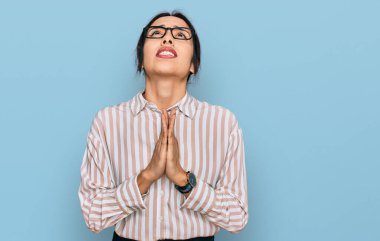 Gündelik kıyafetler ve gözlük takan genç İspanyol kız elleri ile yalvarıyor ve dua ediyor. Yüzünde umut ifadesi var. Çok duygusal ve endişeli. Yalvarıyor. 